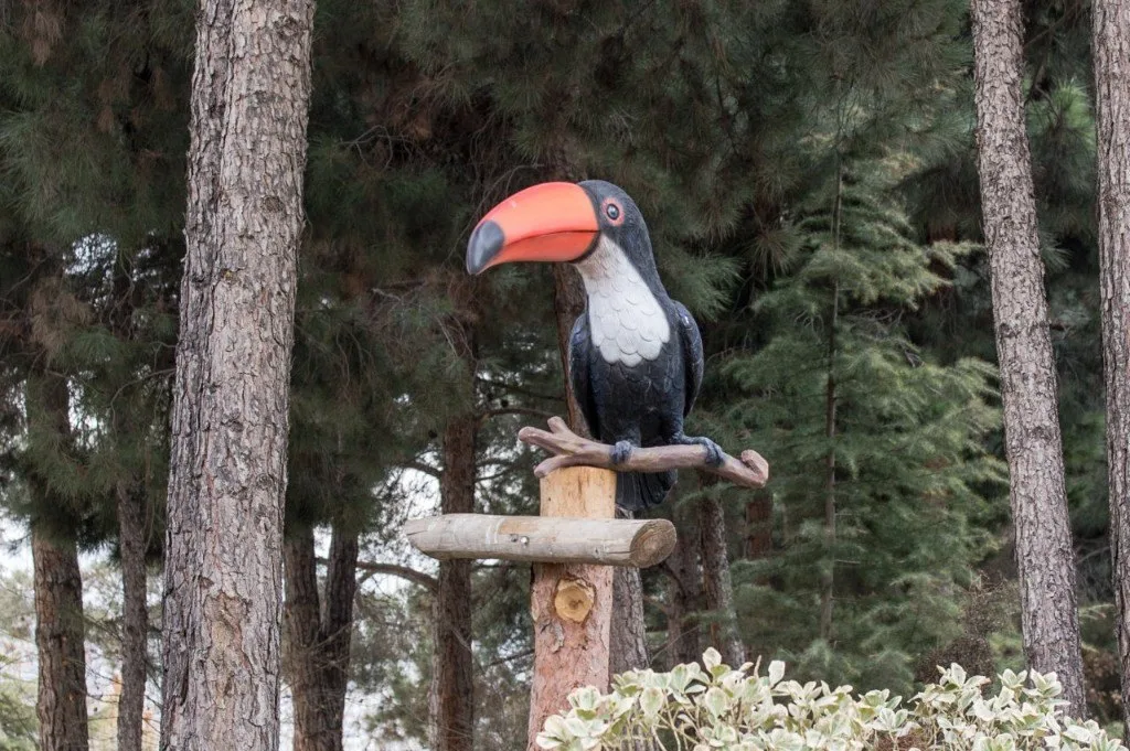 Ein bemalter Tukan auf einem Holzpfosten zwischen Kiefern.